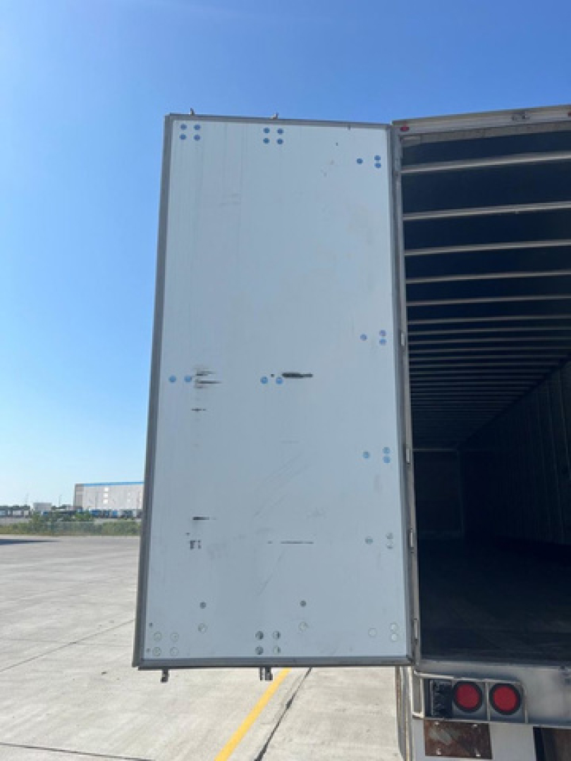 Trailer side door of a white utility van trailer with riveted seams and a dark interior, visible hinges and rear lights.