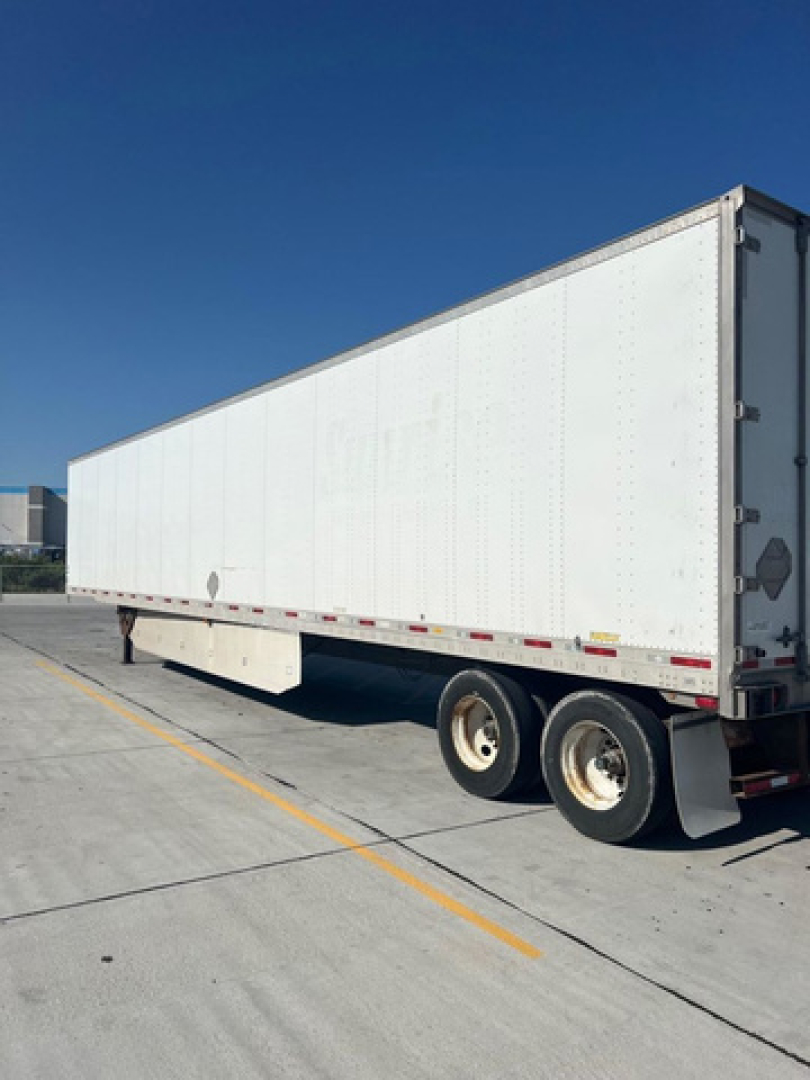 White trailer with dual rear wheels; side view shows smooth white panels and small round door mirror; rear bumper and reflective tape along side.