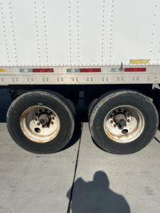 Dual rear trucks on a used 2014 utility van trailer showing two wheels and part of the aluminum ribbed side with reflective tape.