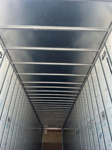 Trailer interior showing vertical side walls and ceiling ribs in a cargo van/trailer. Narrow long view toward back with metallic framework and numbers along sides.