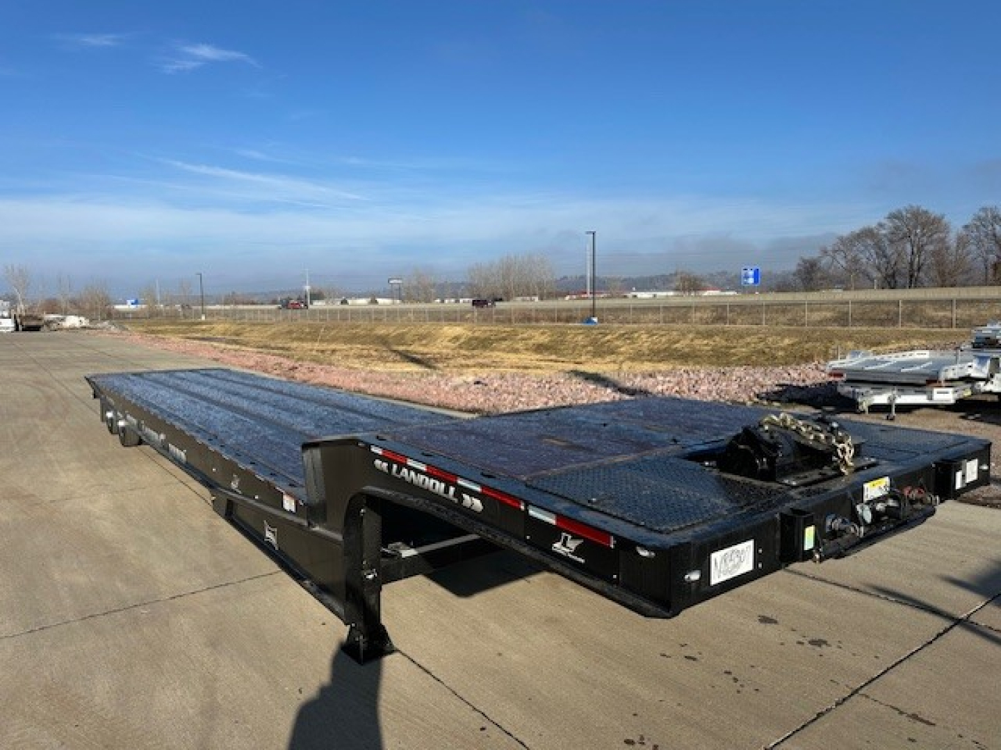 Equipment trailer showing a long black Landoll 440 flatbed trailer with a gooseneck, parked on a lot with clear sky.
