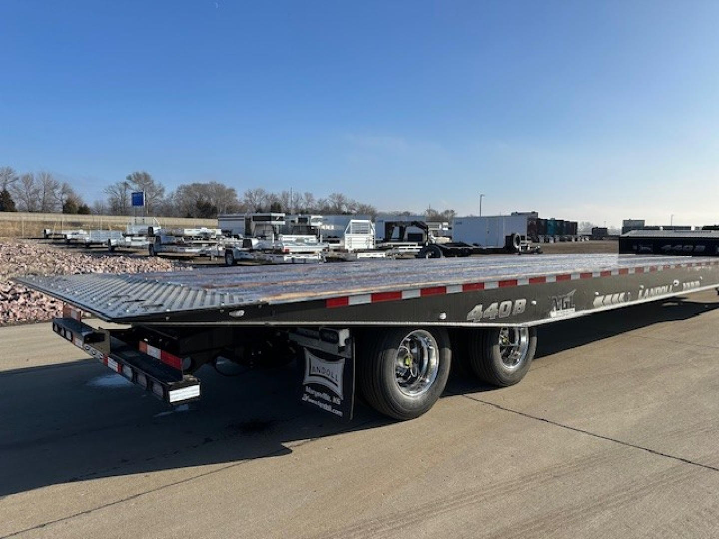 Landoll 440 trailer showing long steel deck with dual rear axles and wheel wells, flatbed design, side reflectors, and branding along the side.