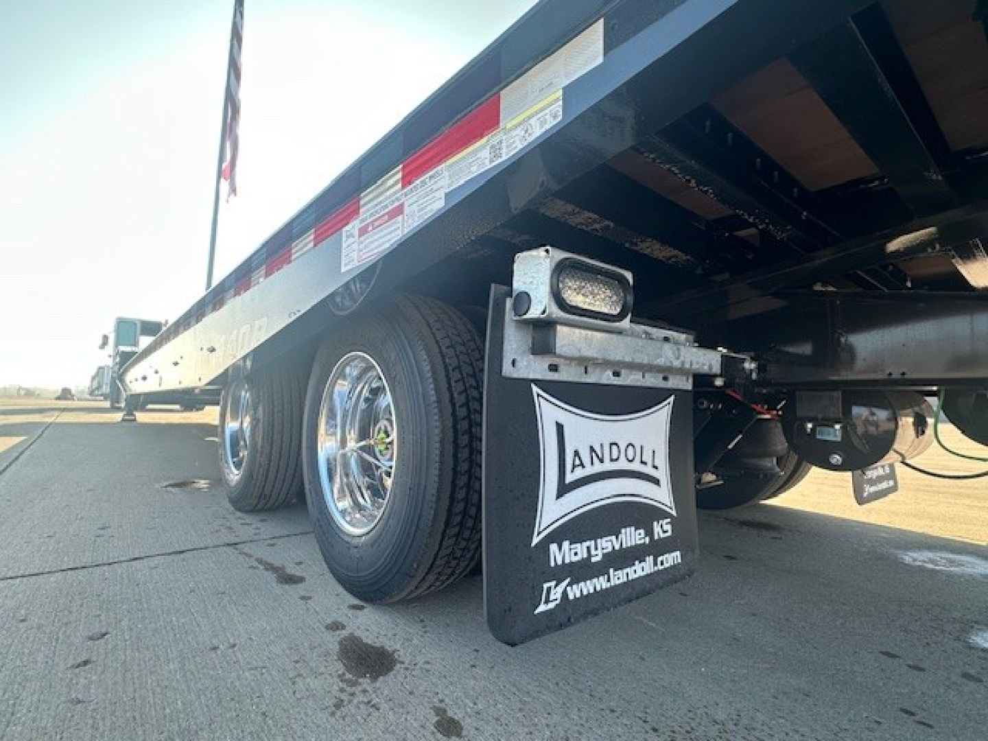 Trailer undercarriage with dual rear axles and Landoll mudflap showing Andoll logo and Marysville, KS; visible tires, deck side rails, and reflective safety decals.