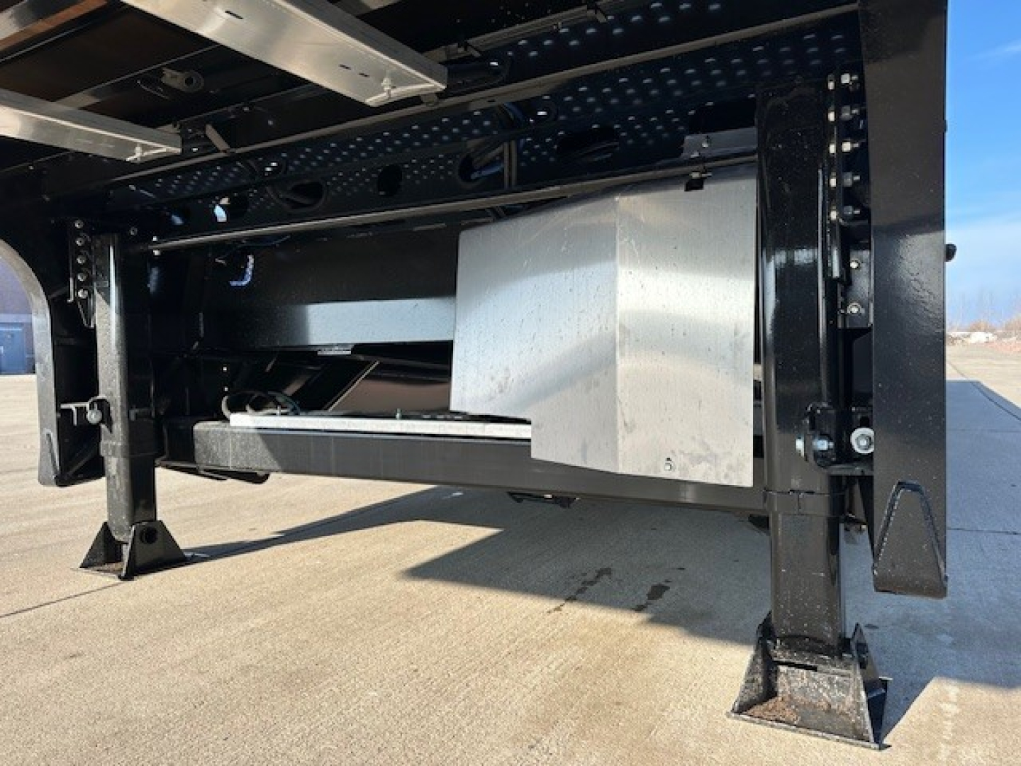 Underframe of a Landoll trailer showing structural beams, black-painted steel, and a large metallic box/drawer assembly inside the frame.
