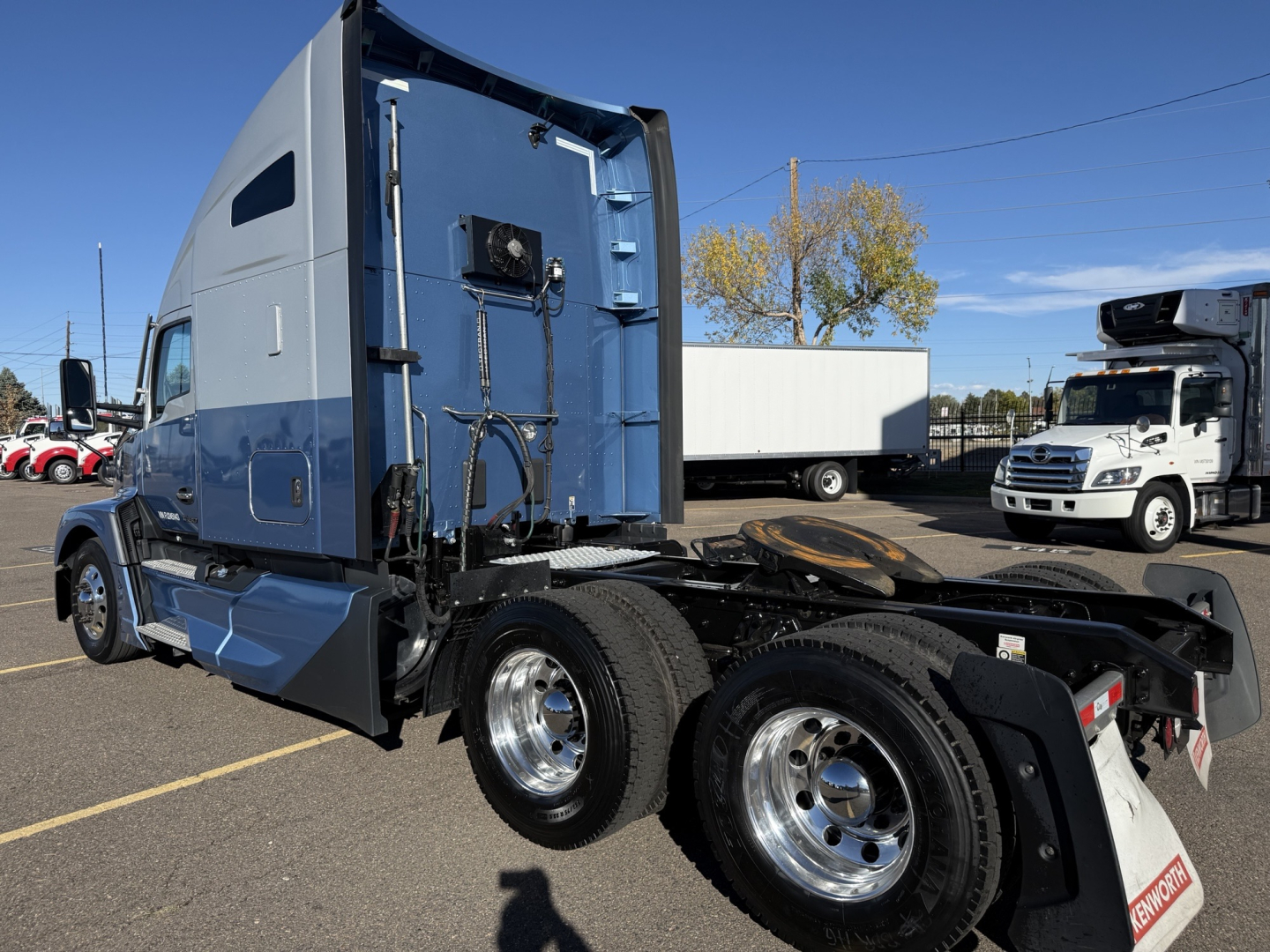 Kenworth T680 tractor cab visible from rear-side view, with blue cab, dual rear axles, chrome wheels, and fifth wheel hitch.