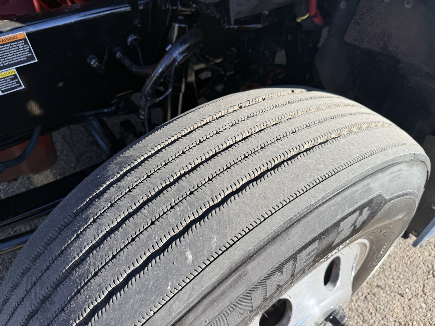 Kenworth T680 wheel and tire close-up showing front axle and suspension area with tire tread visible.
