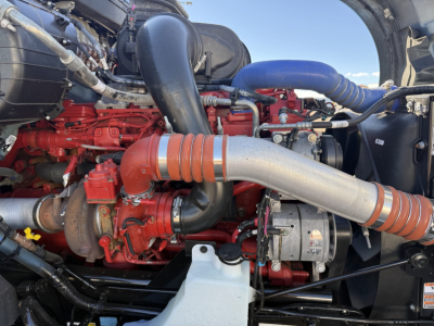 Kenworth T680 engine bay showing red engine components, large silver exhaust duct, blue hoses, and black intake piping.