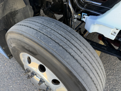 Kenworth T680 front wheel and suspension area showing a large single steer tire with tread, wheel and hub, and partial undercarriage components.