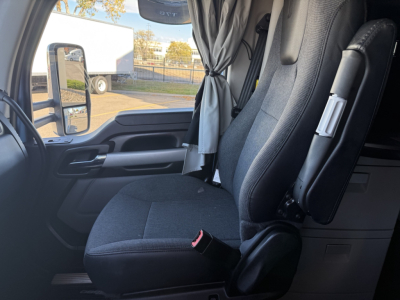Cab interior of a Kenworth T680 in-view front seat area, showing driver seat, window with side mirror, and sun shade.