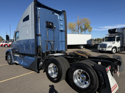 Kenworth T680 tractor cab visible from rear-side view, with blue cab, dual rear axles, chrome wheels, and fifth wheel hitch.