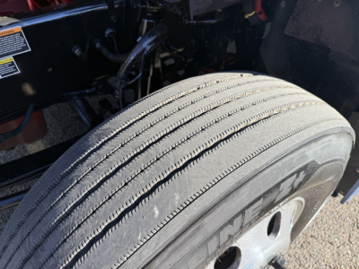 Kenworth T680 wheel and tire close-up showing front axle and suspension area with tire tread visible.