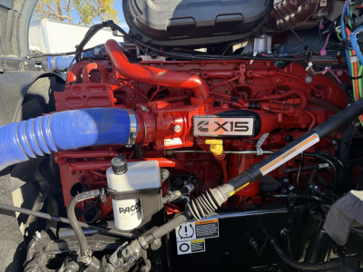 Kenworth T680 engine bay showing X15 badge on red engine and blue intake hose with PACCAR auxiliary reservoir