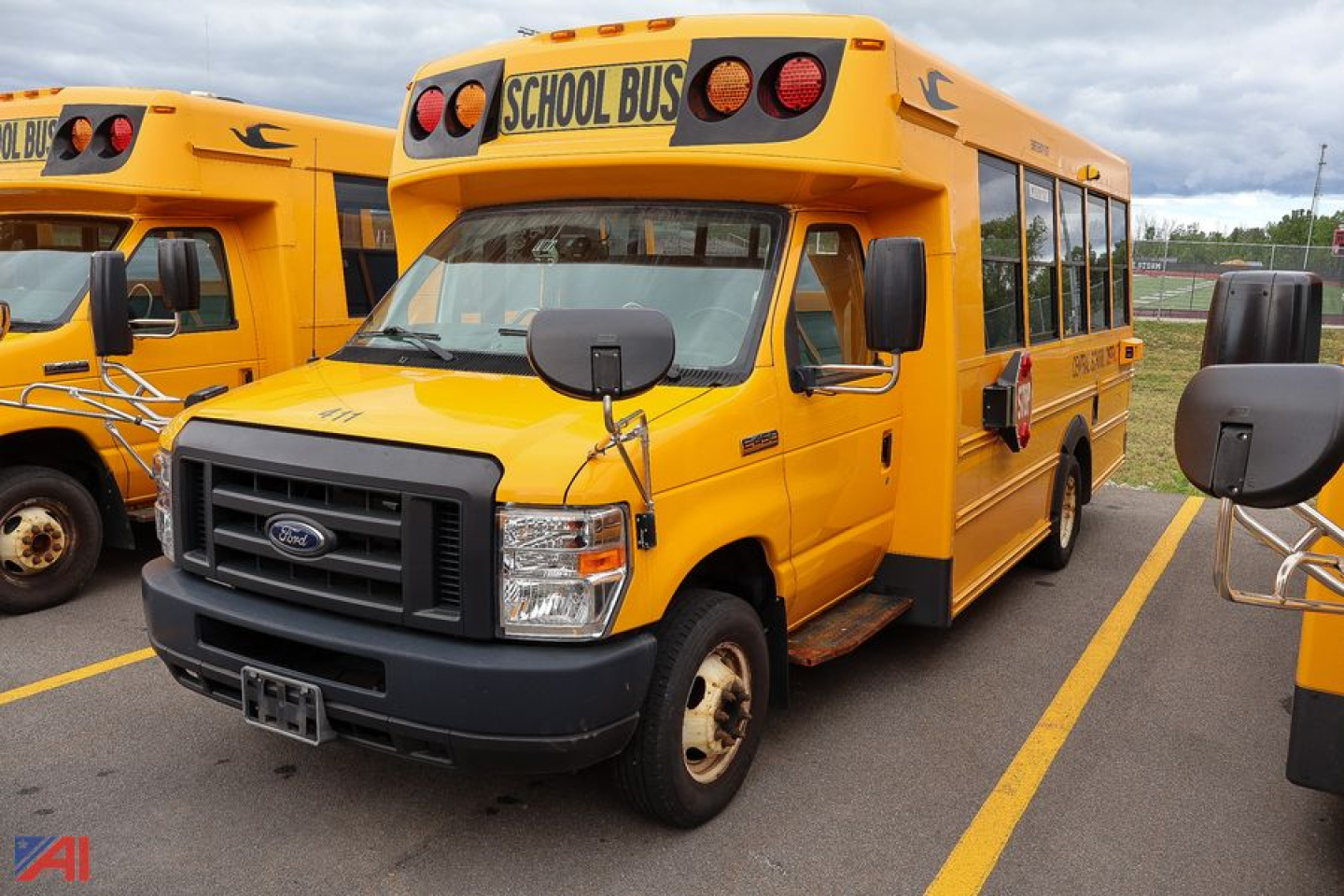 2019 Ford Blue Bird E-Series school bus in yellow, front view showing Ford grille and 'SCHOOL BUS' signage on the roof, side mirrors extended, parked with another bus nearby.