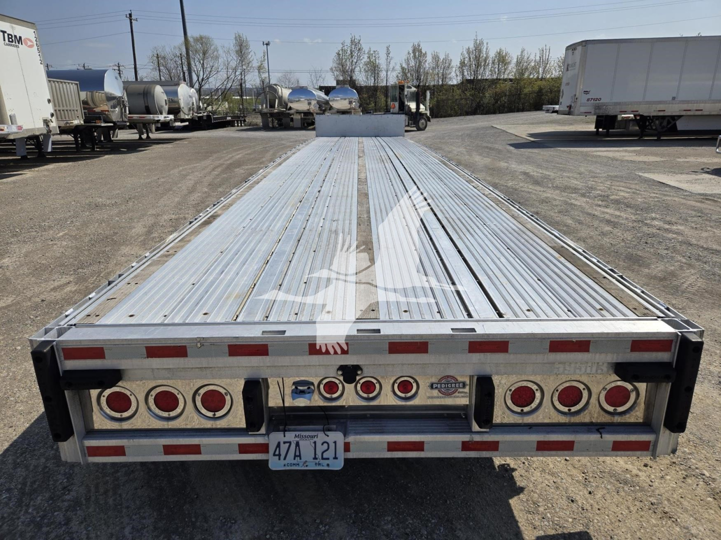 Trailer rear view showing a long aluminum flatbed/deck with multiple circular taillights and a license plate nearby.