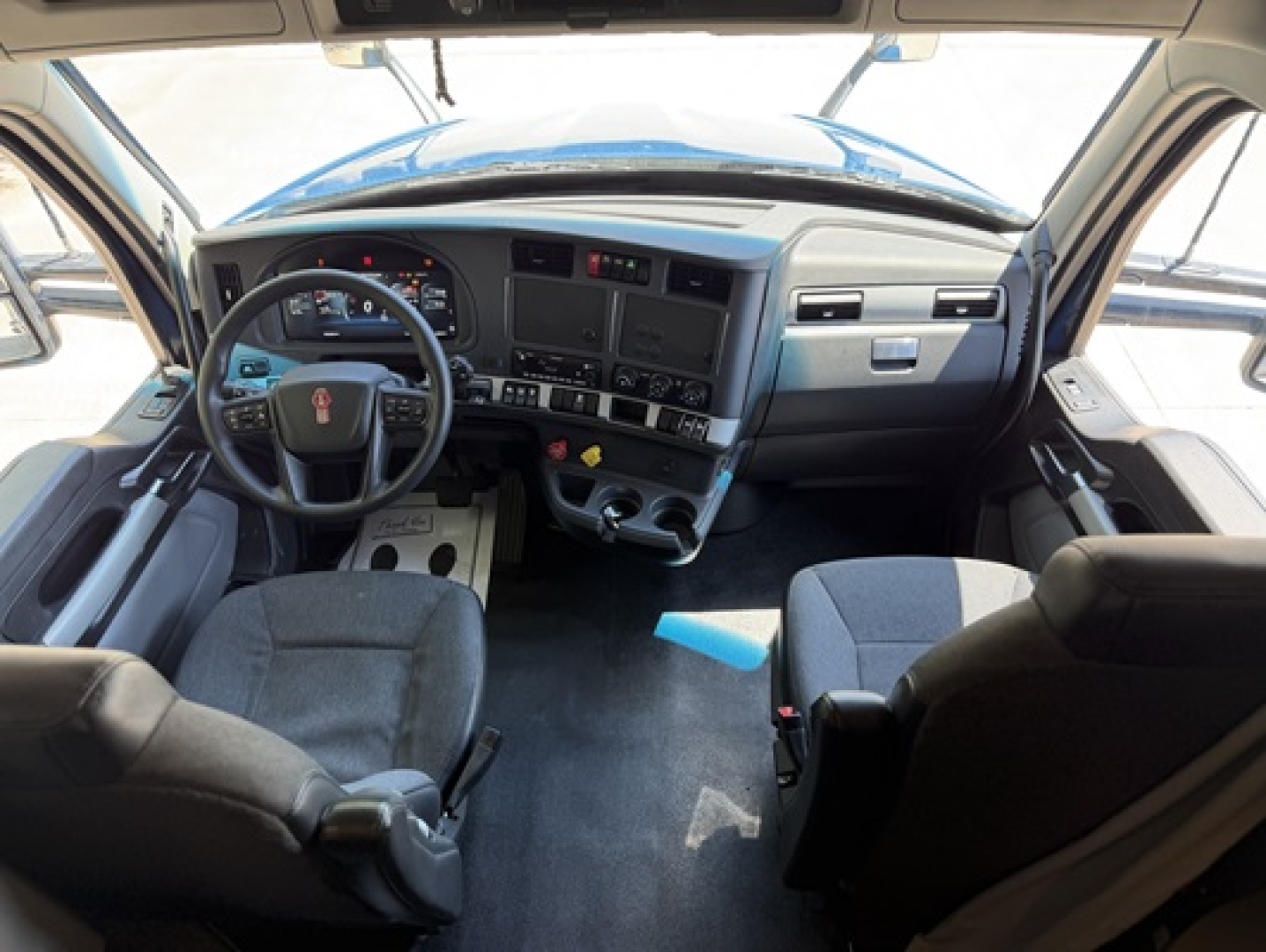 Interior of a Kenworth T680 cab showing dashboard, steering wheel, and front seats.