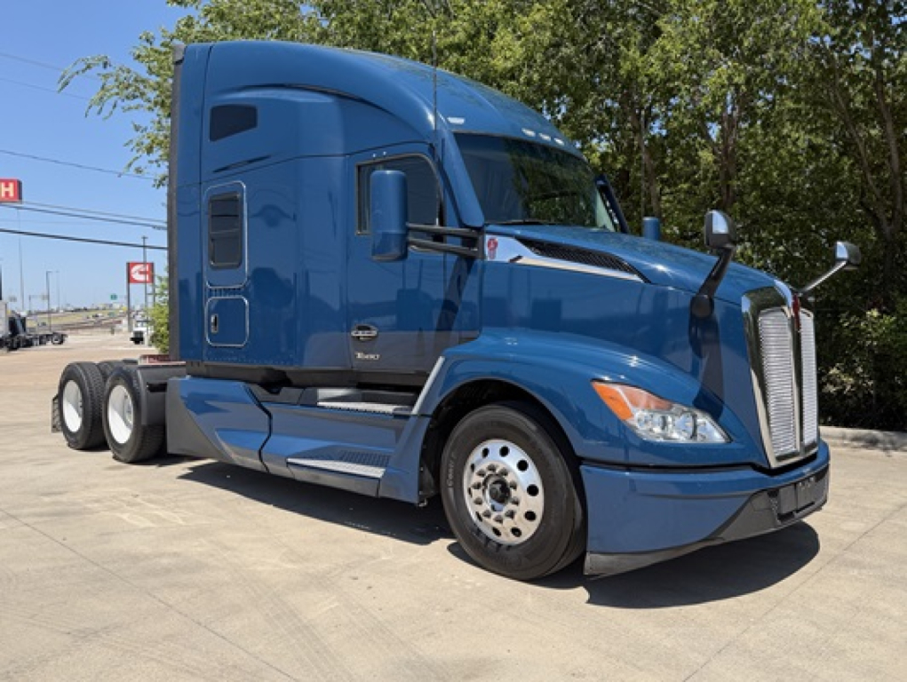 Blue 2023 Kenworth T680 conventional sleeper truck in a parking lot, three-quarter view.