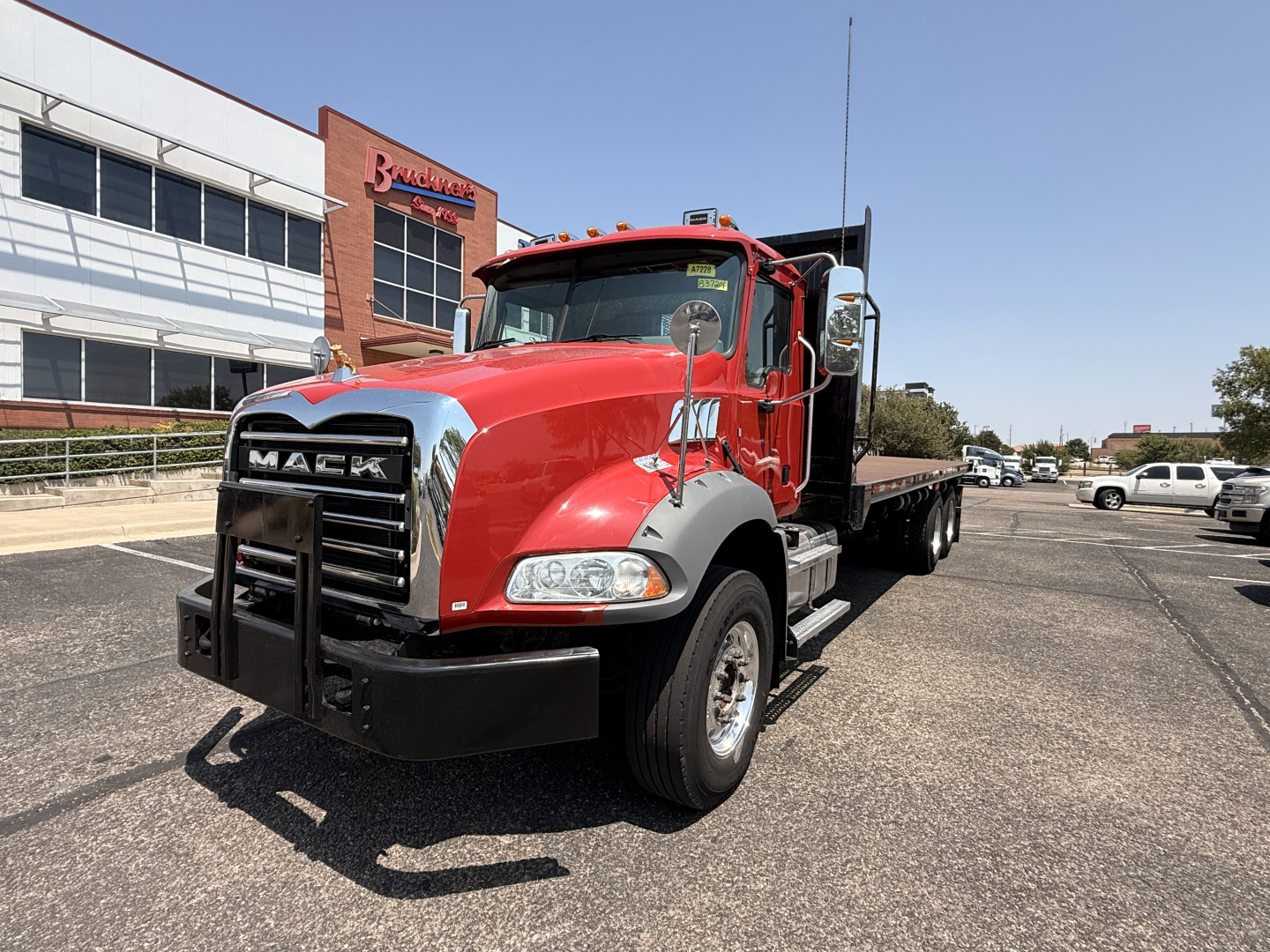 Truck front-left view of a red 2020 Mack Granite flatbed with chrome grille, black bumper guard, and flatbed in background.