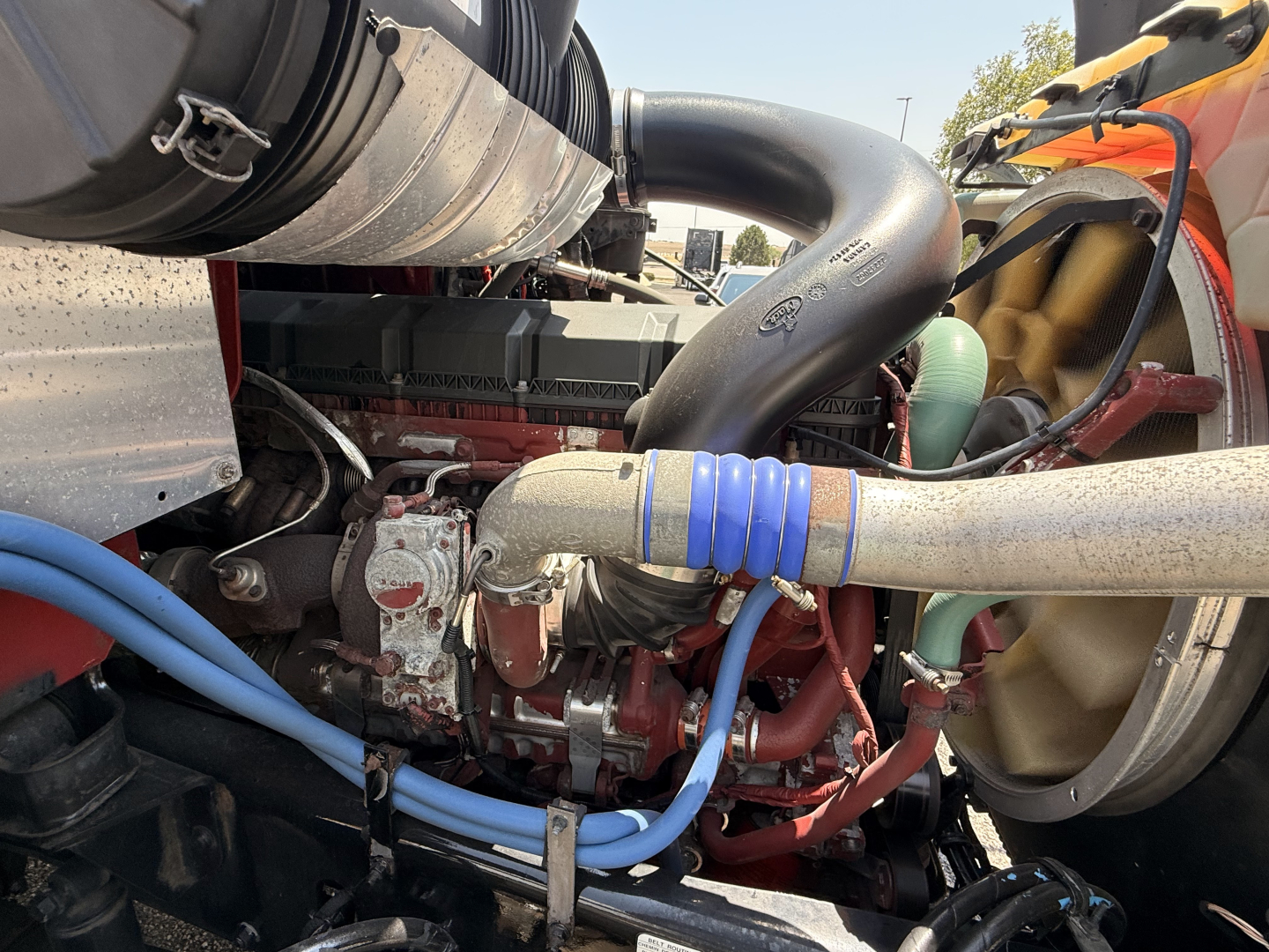Truck engine bay showing coolant hoses, turbocharger intake, and blue quick-connect hoses in a Mack Granite engine under a flatbed.