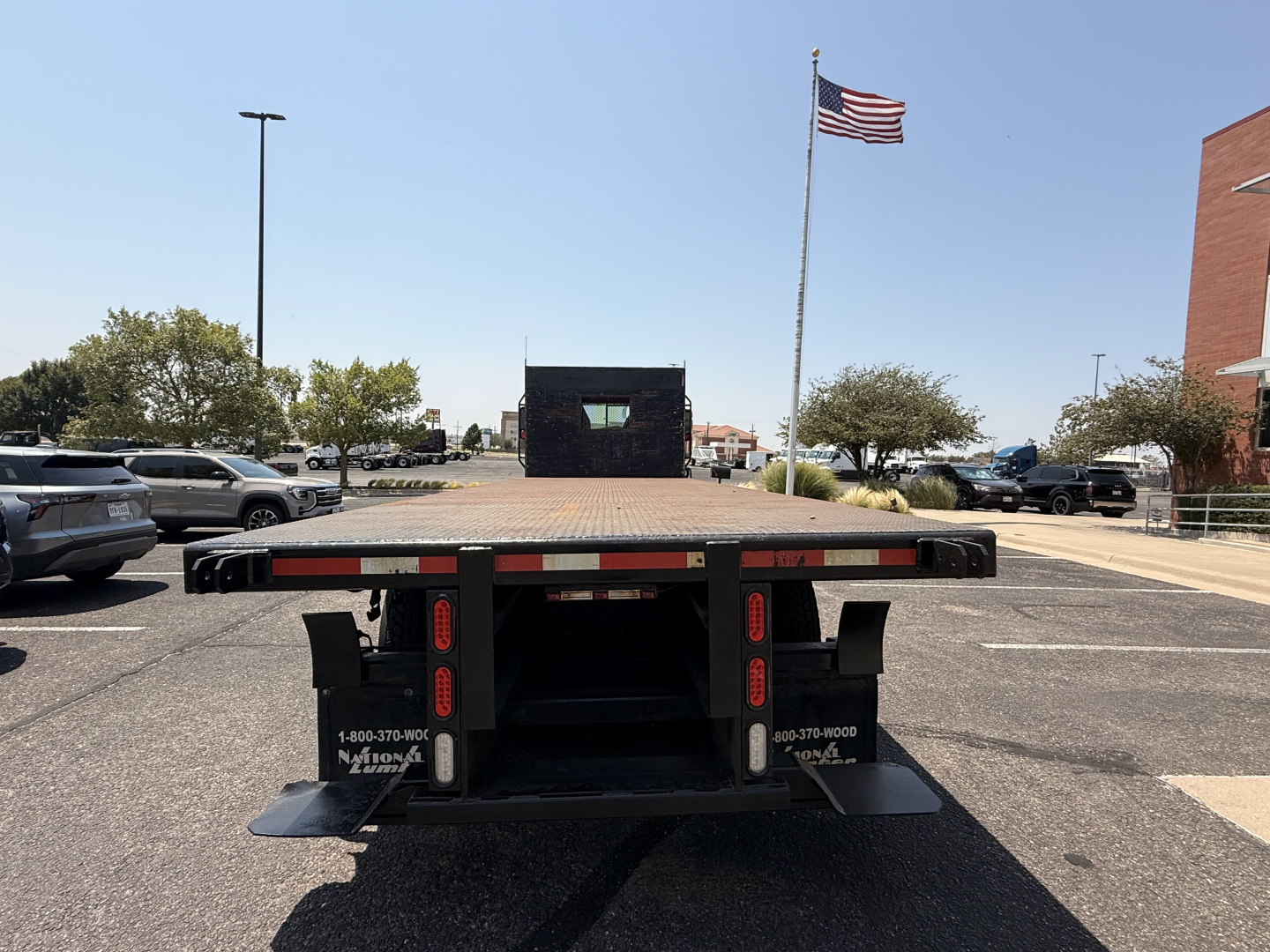 Flatbed truck rear view showing a trailer with red and white reflectors, black frame, two rear lights, and tail supports.