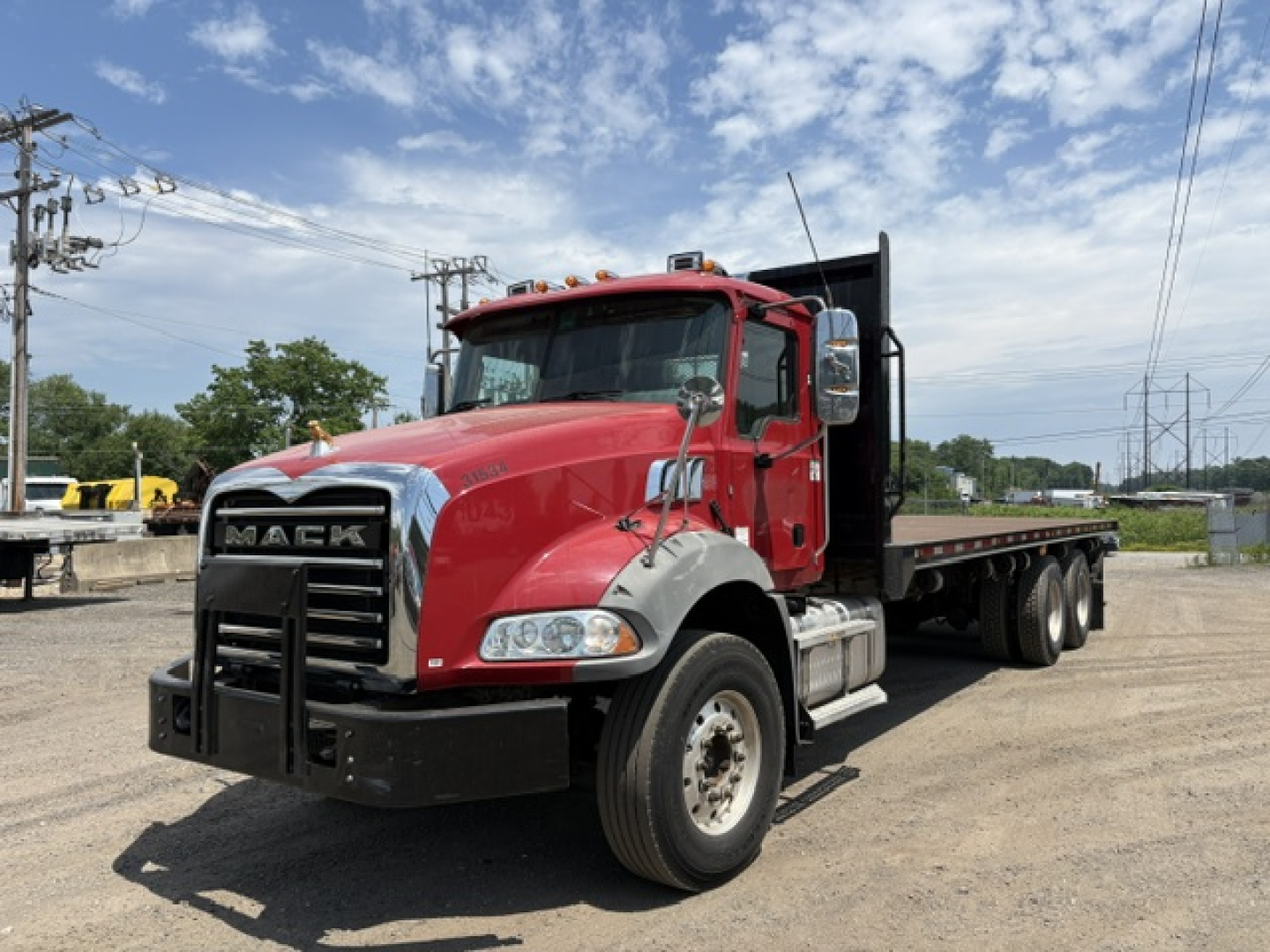 2020 Mack GRANITE dump truck in red cab with black grille and flatbed, side view showing front wheels and dual rear axles on a gravel lot.