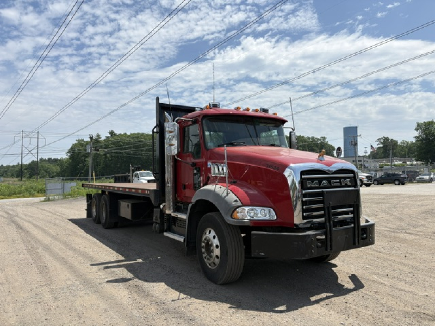 Mack Granite flatbed truck showing front and driver side, red cab, black bumper, and plant steel flatbed in an open lot.