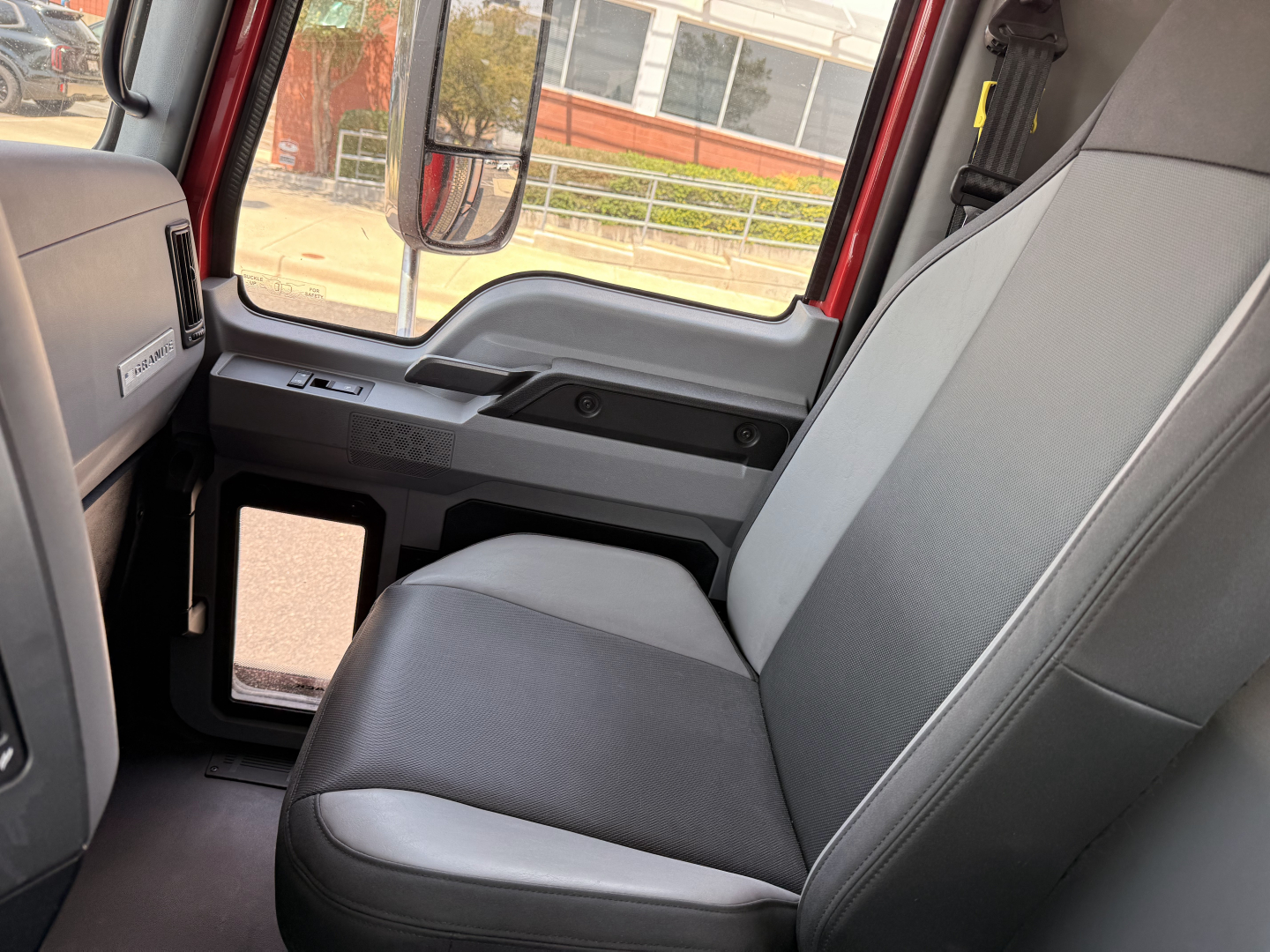 Interior of a Mack Granite truck cab with front passenger seat and door window, showing gray fabric seat, dashboard, and side panel.