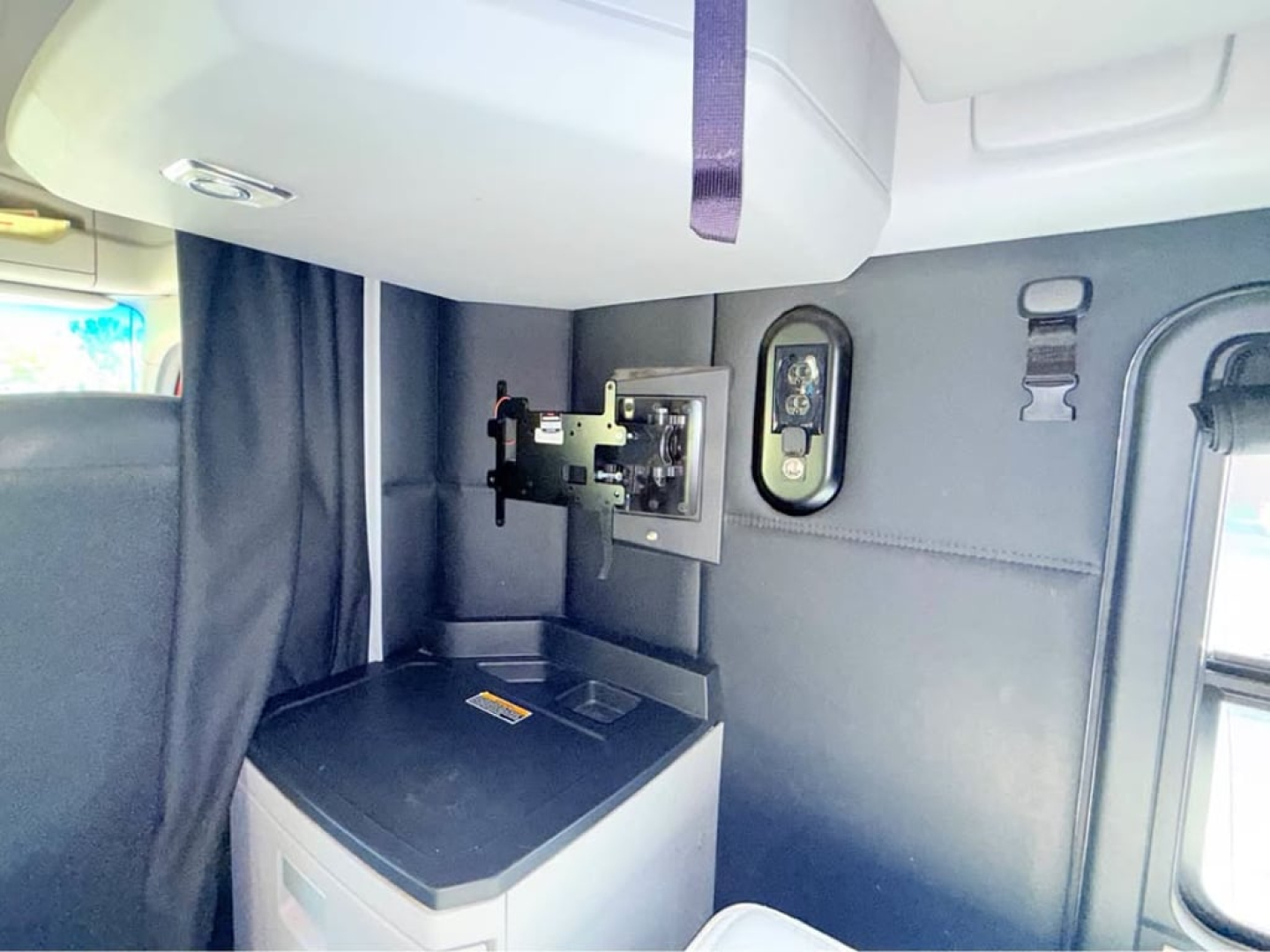 Kenworth T680 sleeper cab interior showing a mounted device bracket and control panel on a dark panel, with a purple strap visible overhead.