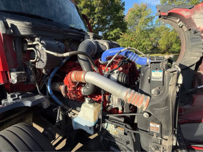 Kenworth T680 engine bay view showing turbocharger and hoses; red engine block, blue silicone hose, black radiator shroud, assorted labels and fluid reservoirs.
