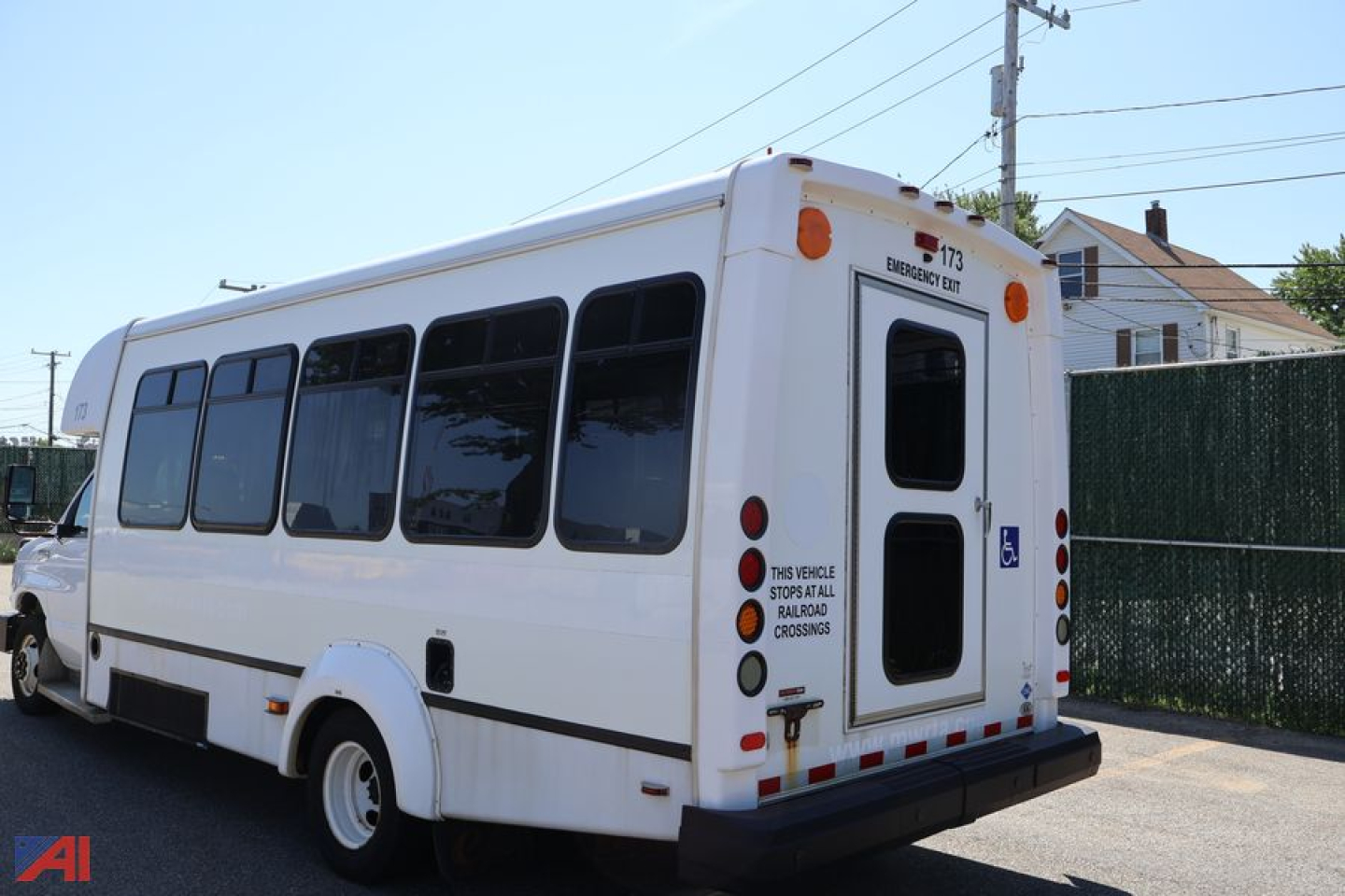 Rear and side view of a white Ford E-450 wheelchair bus with large windows, rear door, and accessibility markings. Visible text includes "173" on top rear, and small signs near back door such as wheel chair symbol and safety notices.