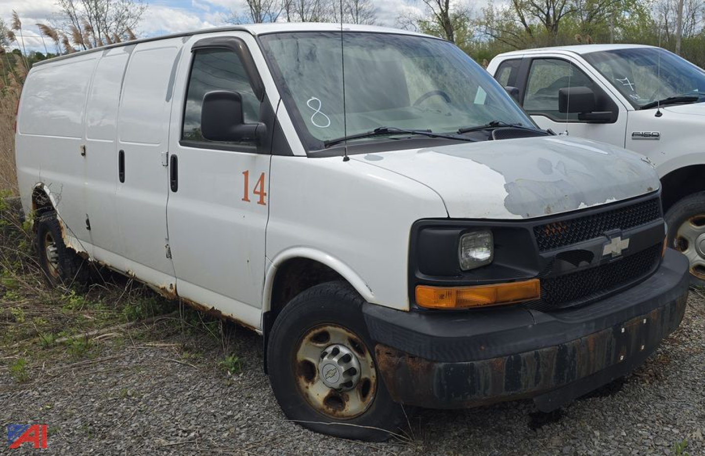 Chevrolet Express 3500 cargo van, white, side view showing orange '14' on door, rust on wheel area, front grille with Chevrolet emblem, plain utility van in salvage lot.