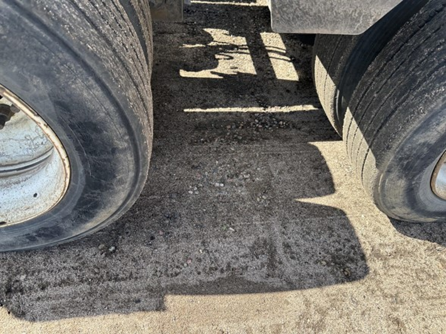 Trailer axles and dual tires of a Load King lowboy trailer showing mud and gravel undercarriage surfaces.