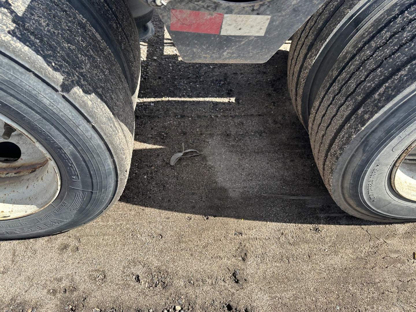 Trailer dual rear tires of a Load King lowboy with West Coast spreader bar, showing tires and dirt on the frame.