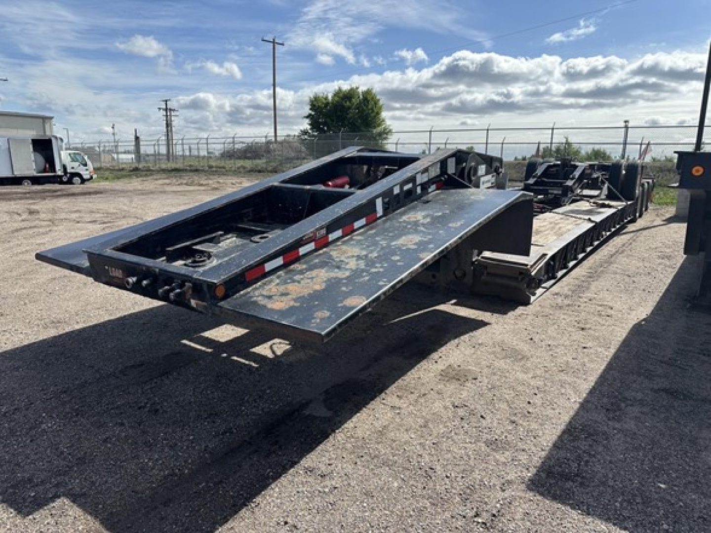Trailer deck on a Load King lowboy trailer with extended flatbed and hydraulic ramps, side rails, and worn surface.