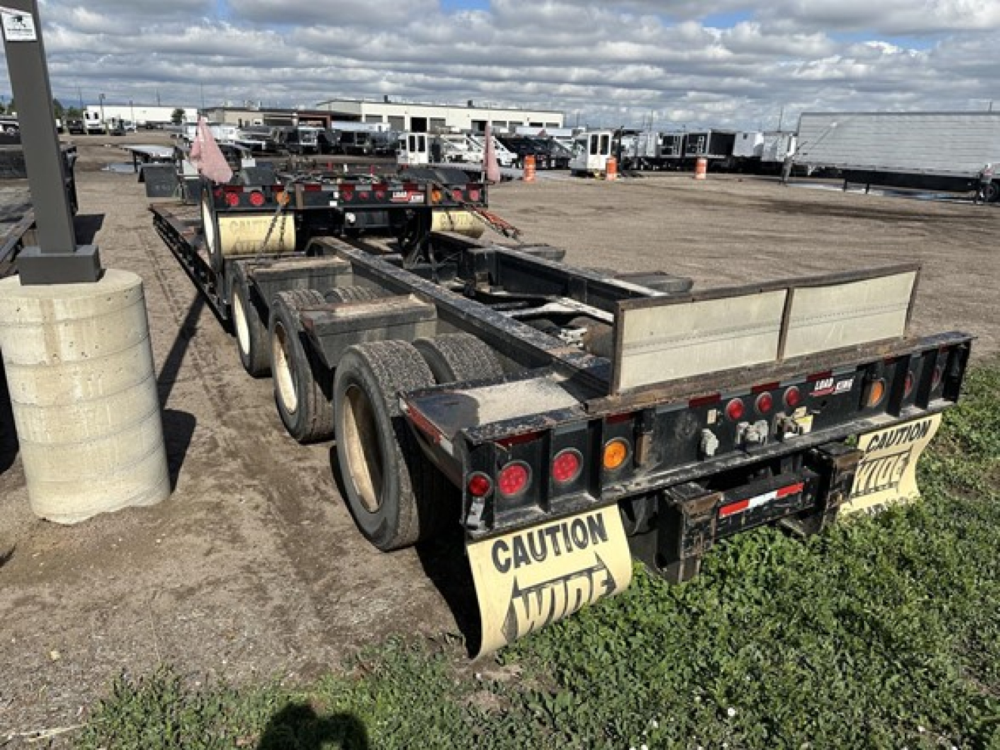 Trailer rear view of a used Load King lowboy trailer with dual rear axles and safety mud flaps reading CAUTION WIDE, showing rear lights and metal bed.
