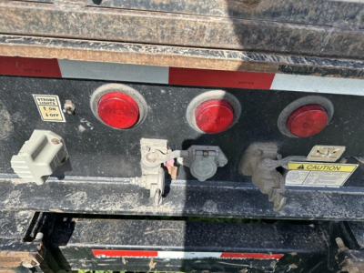 Trailer rear showing control lights and hydraulic connections with warning labels and electrical sockets.
