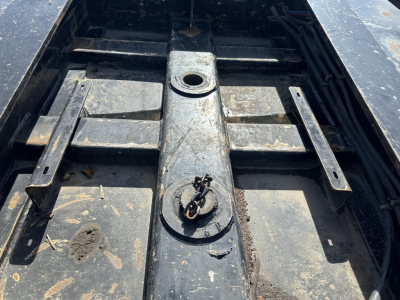 Trailer bay showing mounting bracket and coupling area on a Load King lowboy trailer with West Coast spreader bar and debris on metal surface.