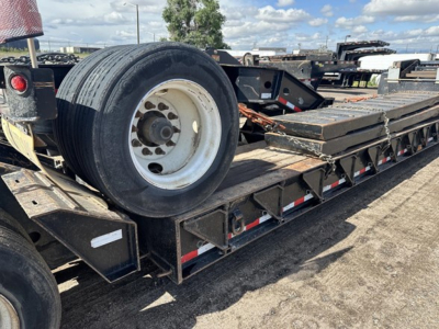 Trailer deck of a Load King lowboy with a spare tire mounted on the side and steel side rails, showing a long flatbed and ramp sections.