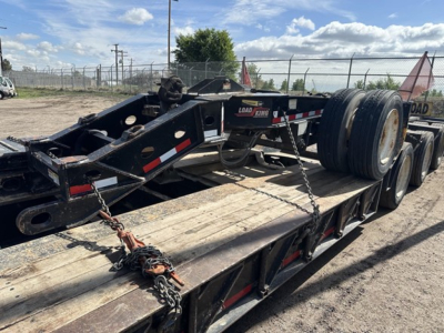 Load King lowboy trailer frame showing dual rear axles and chain securing straps, with faded black paint and red/white reflective markers.