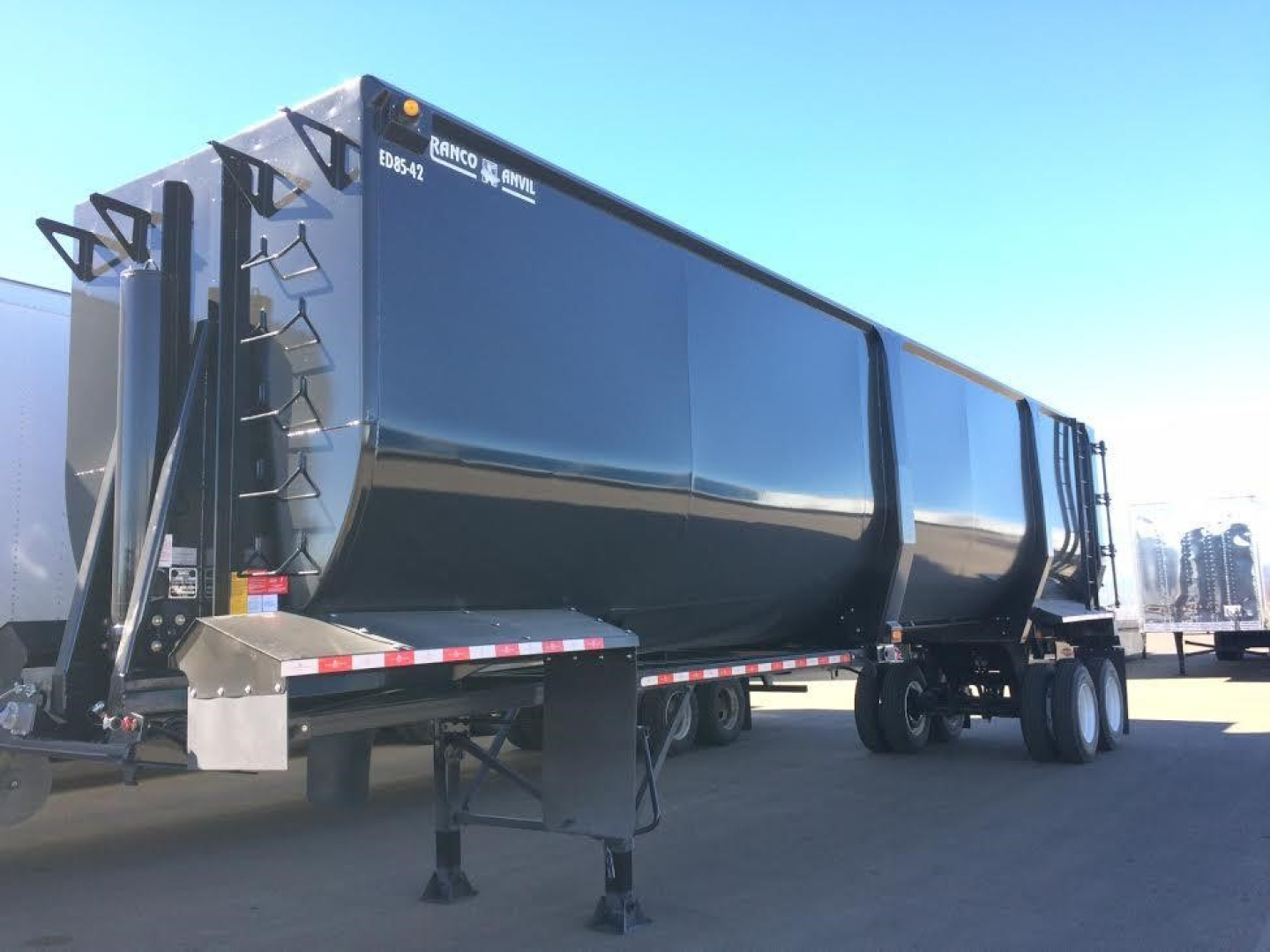 Ranco Ed85-42 dump trailer in service bay with black exterior and front ladder, showing manufacturer markings along top edge.