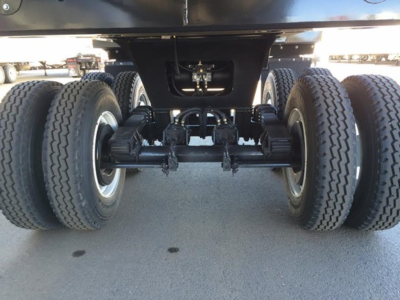 Trailer rear axles showing dual dual-wheel setup and suspension components under the frame of a dump trailer.