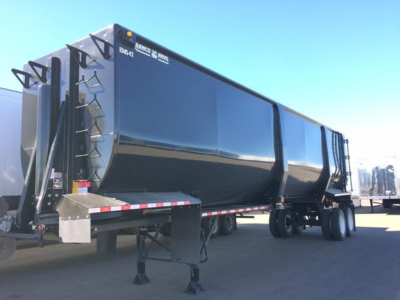 Ranco Ed85-42 dump trailer side view showing ED85-42 marking and ladder brackets on the front; large black dump body with tandem axles and support legs.