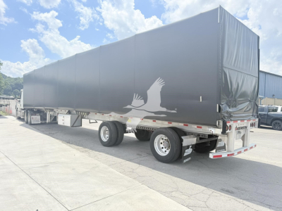 Curtainside trailer with black cover showing a white crane logo and blank sides; rear and side view; Benson-Conestoga trailer in used condition.
