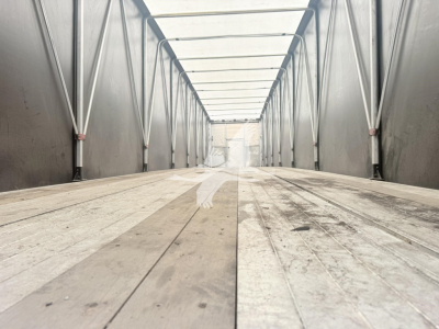 Trailer interior showing a long empty curtain-side trailer with wooden floor, side rails, and internal support frames.