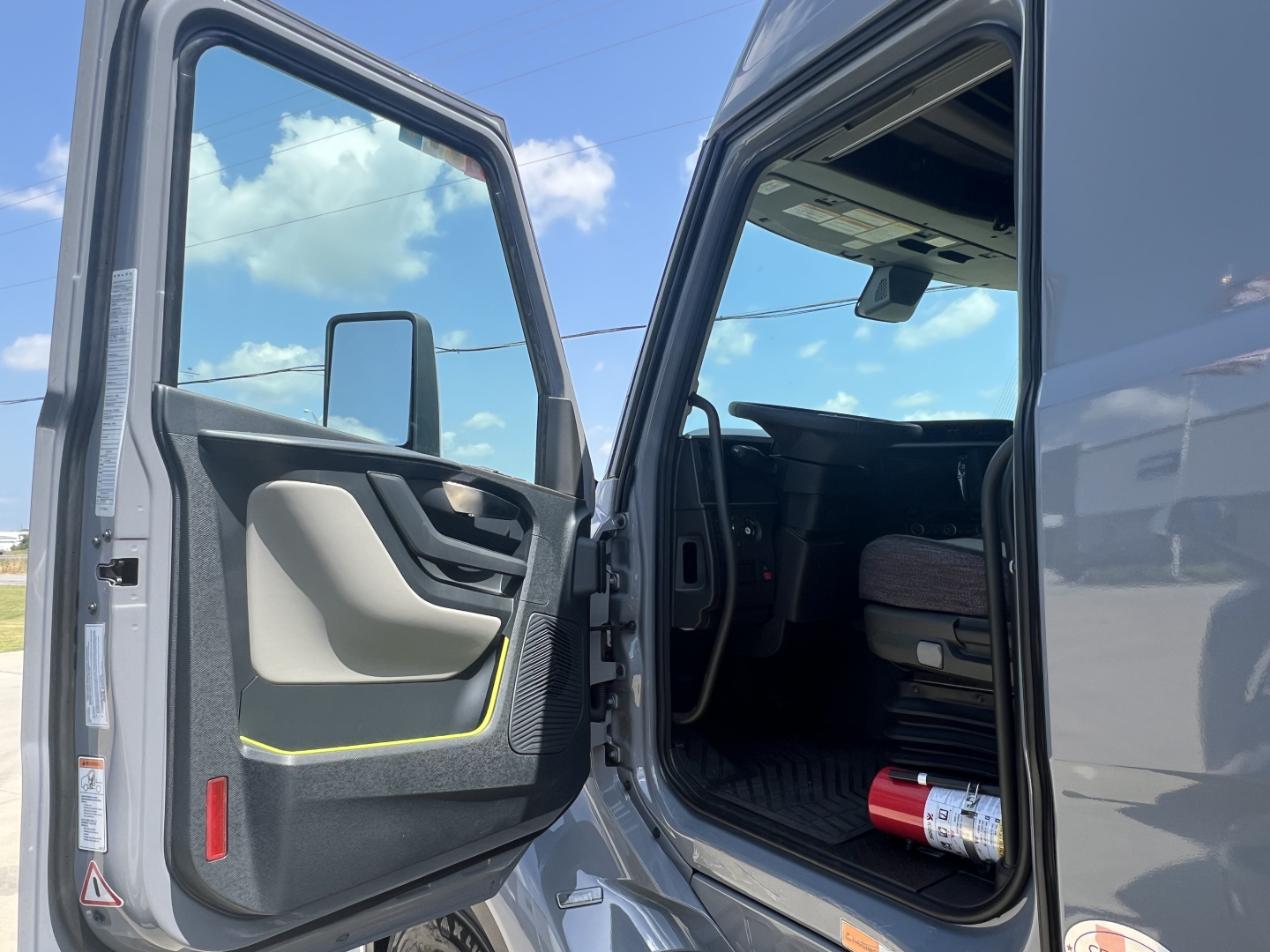 Truck cab interior with open door, view of driver seat and dashboard, exterior gray cab.