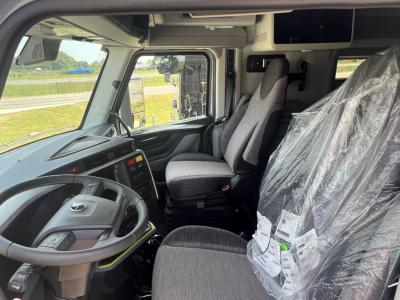Volvo VNL64T860 cab interior showing driver seat and passenger seat with plastic-wrapped components and dashboard controls.