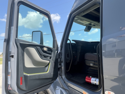Truck cab interior with open door, view of driver seat and dashboard, exterior gray cab.