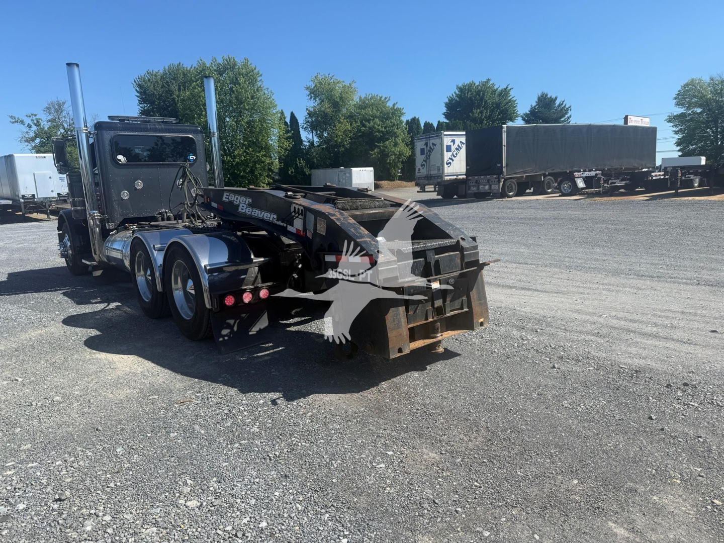 Lowboy trailer showing hydraulic arm and rear hook area with tires and chassis visible.