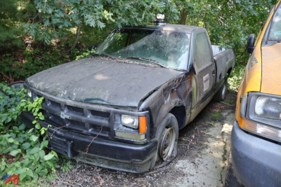 1993 Chevrolet C/K 1500 Series pickup truck in overgrown lot with damaged front left fender and windshield.