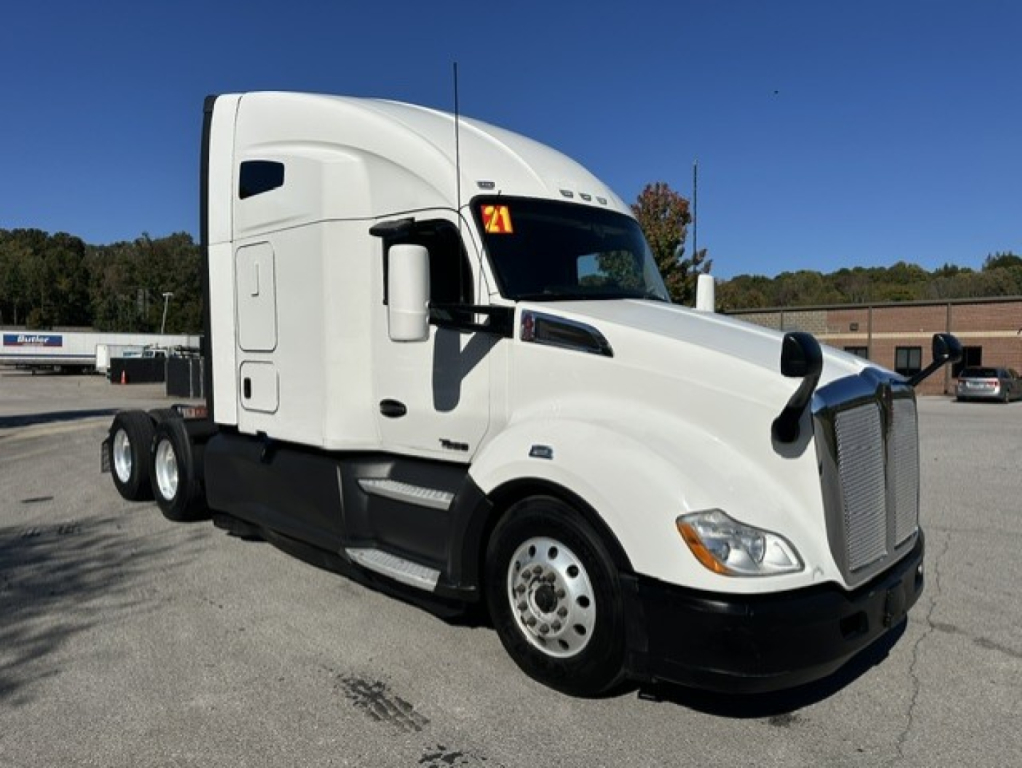 Kenworth T680 model truck visible with sleeper cab, white exterior, three rear axles, front view shows hood and grille.