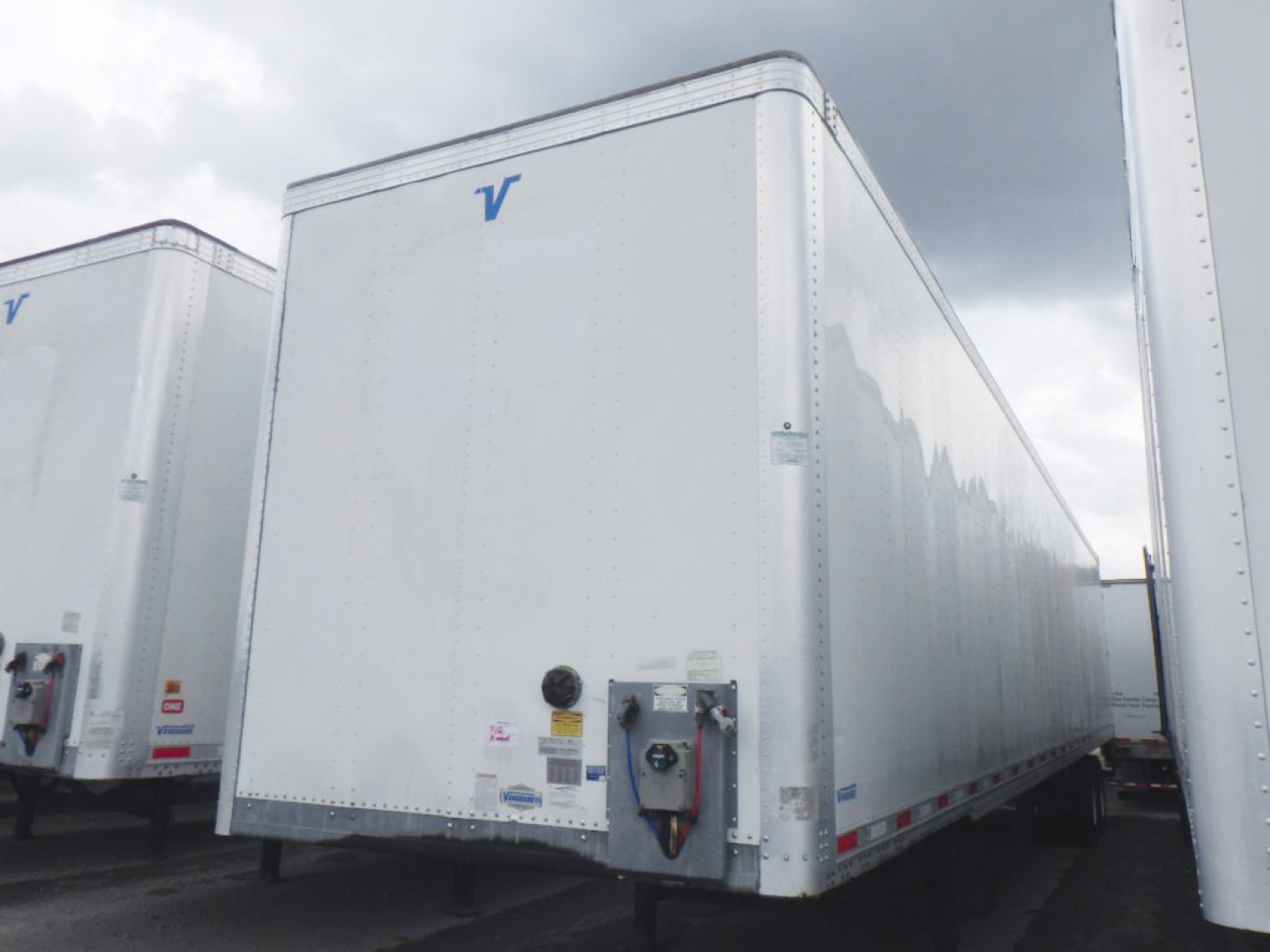 Trailer-aluminum van side showing front corner of a Vanguard box trailer with blue Vanguard logo, front doors, and hitch area.